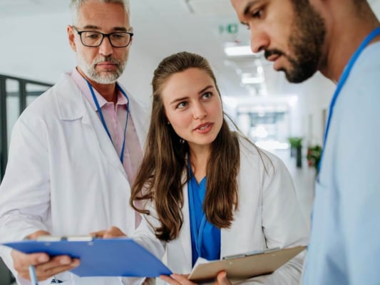 Female doctor speaks to file with two male doctors, all in white coats
